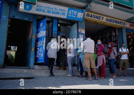 Maskierte Menschen, die sich vor dem Dashain-Festival während der Covid-19-Pandemie in Nepal an einem Geldautomaten in Pokhara anstellen, um Geld abzuheben. Stockfoto