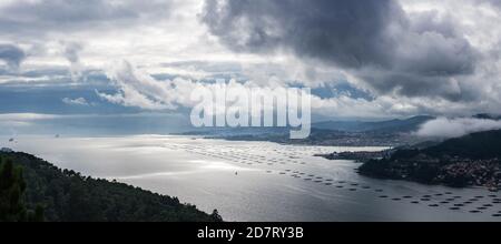 Panoramablick auf die Mündung der Ria de Vigo von Redondela an einem bewölkten Sommernachmittag, mit dem Atlantischen Ozean und den Cíes Inseln auf der linken Seite. Stockfoto