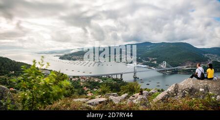 Ein nicht erkennbares Paar genießt den Sonnenuntergang über der Mündung der Ria de Vigo in Redondela an einem bewölkten Sommernachmittag mit der kürzlich erweiterten Rande b Stockfoto