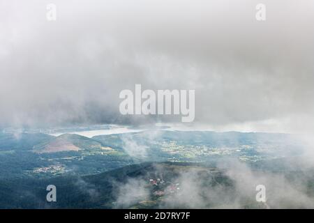 Luftaufnahme der Mündung der Ria de Arousa vom Berg Muralla an einem nebligen Sommernachmittag, mit einigen Windturbinen zwischen den Wolken. Stockfoto