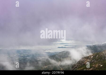 Luftaufnahme der Mündung der Ria de Arousa vom Berg Muralla an einem nebligen Sommernachmittag, mit einigen Windturbinen zwischen den Wolken. Stockfoto