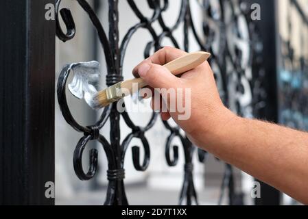 Hand des Auftragnehmers mit Pinsel, die Metallzaun malen. Stockfoto