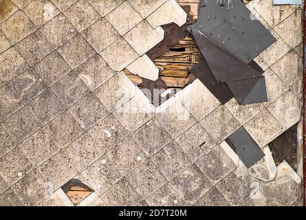 Altes beschädigtes Dach mit Asbestschindeln, die repariert werden müssen. Verschmutzte Balken und zerrissene Abdichtung des Dachmaterials. Stockfoto