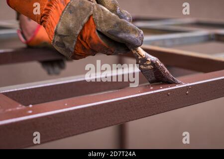 Hand des Auftragnehmers mit Pinsel, die Metallkonstruktion lackieren. Stockfoto