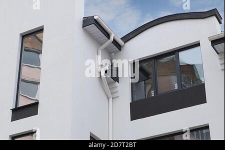 Rahmenhaus Regenrinne System. Weiße Dachrinne auf dem Dach des Hauses. Bau eines neuen modernen Hauses.Neu installierte Regenrinne auf Hausdach Stockfoto