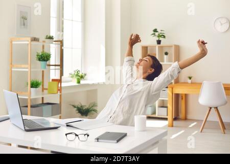 Geschäftsfrau, die am Schreibtisch sitzt, Pause von der Arbeit macht und steife, angespannte Muskeln streckt Stockfoto