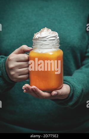 Die Hände der Frau halten ein Einmachglas mit einem Kürbis Latte Stockfoto