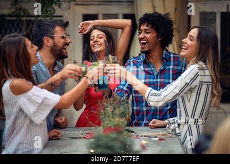 Fröhliche Paare, die auf der Open-Air-Geburtstagsparty in einer schönen Sommerdämmerung anstoßen. Qualität Freundschaft Zeit zusammen Stockfoto