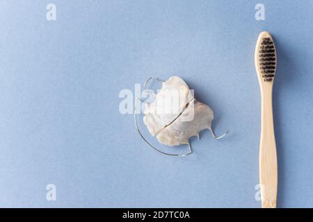 Herausnehmbare kieferorthopädische Platte und Bambus-Zahnbürste auf blauem Hintergrund. Stockfoto