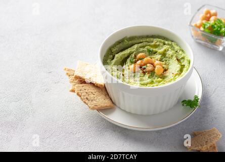 Weiße Schüssel mit Avocado Hummus mit Kichererbsen, Petersilie, Gewürzen und Kräckern Stockfoto
