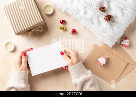 Frauen Hände halten leere Karte und Weihnachtsdekorationen auf beigem Hintergrund. Stockfoto