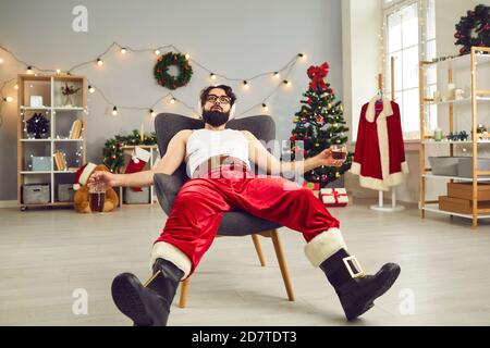 Junger Mann, der Alkohol trinkt und sich nach dem Feiern im Sessel entspannt Es war an der Weihnachtsnacht sehr hart Stockfoto