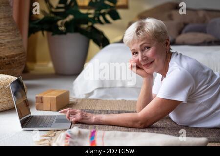 Aktive ältere Frau surfen im Internet auf Yoga-Matte. Stockfoto
