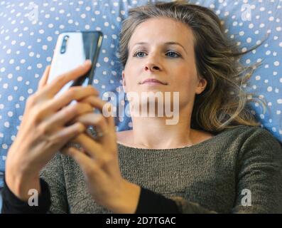 Frau liegt im Bett und überprüft ihr Smartphone nach dem Aufwachen. Stockfoto