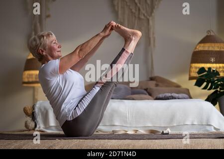 Aktive ältere Frau, die Yoga-Training zu Hause macht, hält navasana oder Boot Yoga Pose Stockfoto