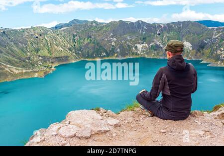 Junger männlicher Rucksacktourist mit Landschaft des Quilotoa Vulkanasees auf dem höchsten Gipfel auf 3930m Höhe entlang der Quilotoa Loop Wanderung, Quito, Ecuador. Stockfoto