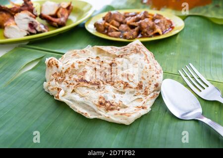 Roti Canai oder Paratha serviert auf Bananenblatt, mit Hammelcurry und gebratenem Huhn Stockfoto