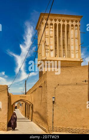 YAZD, IRAN - 27. APRIL 2015: Eine nicht identifizierte Frau geht durch die engen Straßen von Yazd im Iran Stockfoto