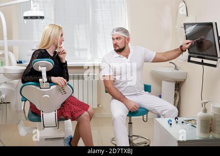 Zahnarzt, der mit dem Patienten spricht und auf einen leeren Monitor zeigt Stockfoto