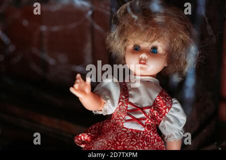 Alte Puppe mit gruseligem Look in rotem Kleid mit blauen Augen und mit Spinnennetz vor ihr. Halloween-Konzept Stockfoto