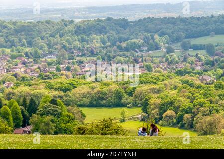 Menschen, die auf Gras sitzen und den Blick auf die Vorstadt Reigate vom Reigate Hill im grünen Gürtel Londons aus betrachten. Stockfoto