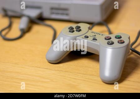 Ein Controller für die ursprüngliche Playstation, angeschlossen an die Konsole, auf einem Holzboden. Stockfoto