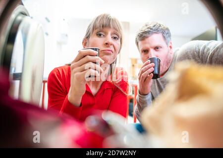 Ein Paar schaut in die Waschmaschine mit Kaffeetasse Stockfoto