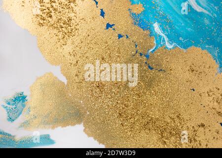 Stapel von Goldpailletten auf blauen Farbflecken. Abstraktes Muster. Stockfoto