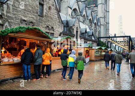 Weihnachtsmarkt in Gent, Belgien. Spaziergänger, weihnachtskioske, Pavillons und Kirche im Hintergrund. Stockfoto