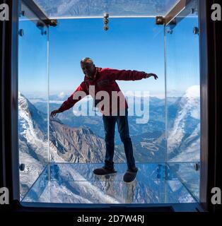 Tourist steht in der Glasbox "Step into the Void" auf dem Gipfel des Aiguille Du Midi (3842m) oberhalb des Mont-Blanc-Massivs von Chamonix, Frankreich. Stockfoto