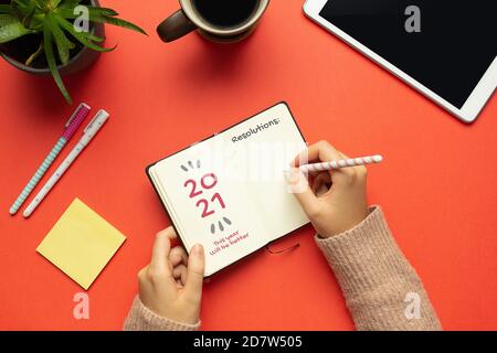 Stock Foto von Frauen Hände schriftlich Auflösungen in einem 2021 Notizbuch für das neue Jahr auf rotem Hintergrund Stockfoto