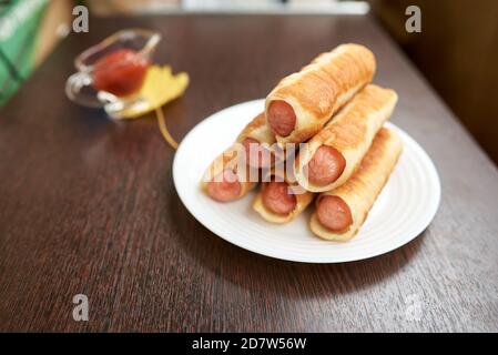 Würste in geröstetem Teig. Gebratene Pasteten mit Würstchen. Sie werden in dünne Streifen Butterteig gewickelt. Stockfoto