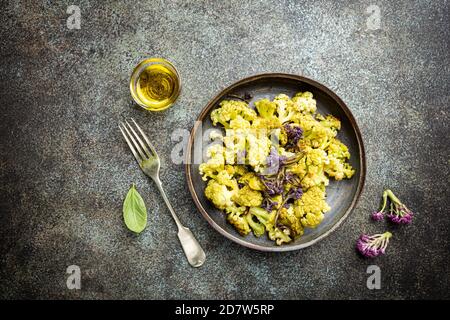 Gebratener grüner und lila Blumenkohl mit Kräutern und Gewürzen auf Teller über grauem Steinhintergrund. Draufsicht Stockfoto