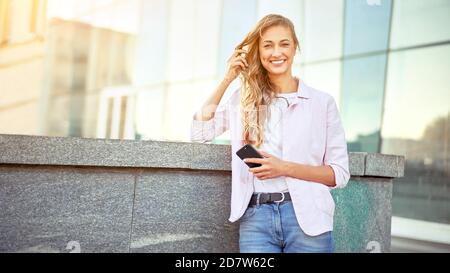 Geschäftsfrau steht Sommertag in der Nähe von Firmengebäude mit Smartphone Zähne Lächelnde Geschäftsfrau im Freien erfolgreiche europäische kaukasische Frau Stockfoto