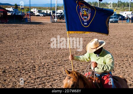 Kleines Rodeo in der Stadt Bryce in Utah USA. Ein Fahrer mit der Utah-Flagge eröffnet die Show. Es mag traditionell sein, aber es ist auch grausam für die Tiere Stockfoto