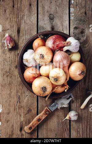 Gelbe, rote Zwiebeln und Knoblauch in einer Schüssel auf Holzgrund. Stockfoto