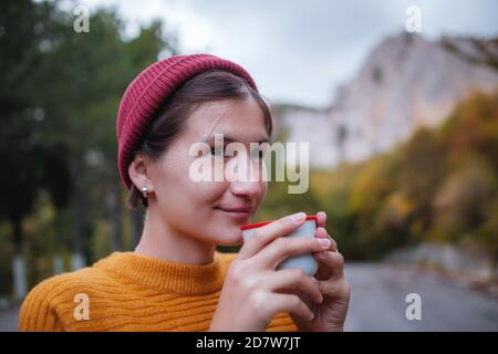 Eine junge Touristin trinkt einen heißen Drink aus einer Tasse und genießt die Landschaft in den Bergen. Trekkingkonzept, warmes Herbstwetter, ruhige Szene. Wandern Stockfoto