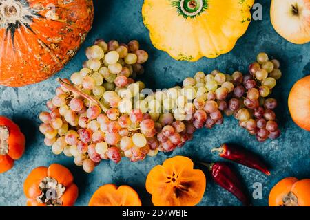 Herbstliches Obst und Gemüse. Ein Bündel Trauben, Kürbis und Kaki auf blauem Hintergrund. Stockfoto