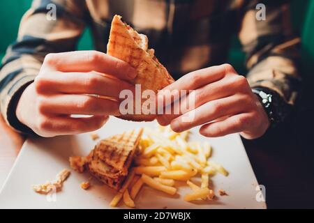 Der junge Mann bereitet sich glücklich, ein saftiges Veggie-Sandwich zu essen. Sandwich aus der Nähe, sichtbare Kichererbsen-Schnitzel, Tomaten und Salat. Stockfoto