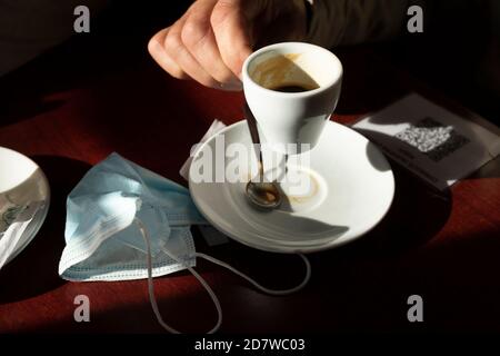Die Hand eines Mannes hält eine Tasse Kaffee, während das Nachmittagslicht durch das Barfenster eintritt, Luesia, Aragón, Spanien. Stockfoto