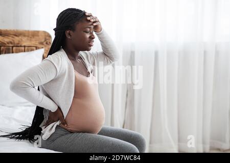 Krank African Schwangere Frau Gefühl Unwohl Zu Hause, Sitzend Auf Dem Bett Stockfoto