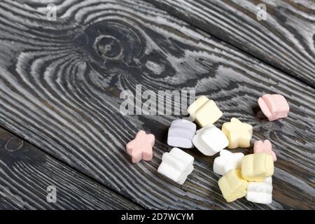 Marshmallows in verschiedenen Farben. Sie liegen auf schwarzen Kiefernbrettern. Stockfoto