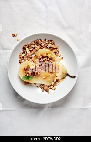 Pochierte Birne mit Joghurt, Walnüssen und Hafergranola. Stockfoto