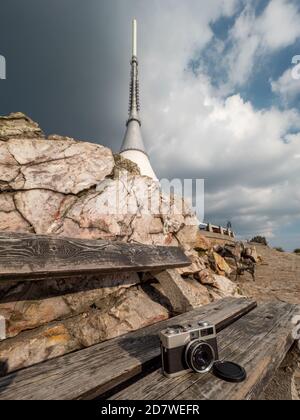 Bank mit Analogkamera und Jested Tower. Das einzigartige architektonische Gebäude. Hotel und TV-Sender auf dem Gipfel des Jested Berg, Liberec Stadt, CZ Stockfoto