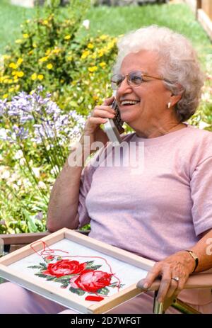 Ältere Frau spricht auf einem veralteten tragbaren Push-Button-Telefon auf ihrer Terrasse, 190er, USA Stockfoto