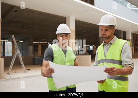 Waist-up-Porträt von zwei professionellen Bauunternehmen Blick auf Pläne, während auf der Baustelle stehen, kopieren Raum Stockfoto
