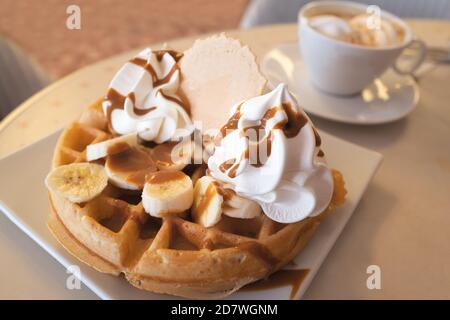 Banane, Karamell und geschlagene Eiscreme Waffel mit einem Wafer neben einem n Espresso Kaffee mit Eis in einer Tasse und Untertasse. Stockfoto