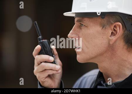 Seitenansicht Porträt eines reifen Arbeiters, der mit Walkie-Talkie spricht Überwachung der Arbeiten auf der Baustelle oder in der Industriewerkstatt Stockfoto