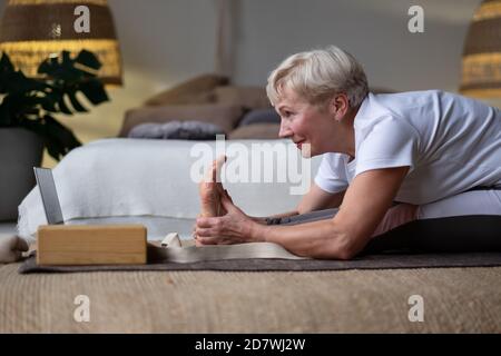 Ältere kaukasische Frau praktiziert Yoga, sitzen in sitzenden vorwärts beugen Übung, paschimottanasana Pose Stockfoto