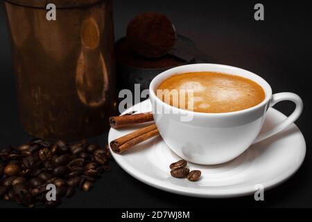 Weiße Tasse Kaffee, Kaffeebohnen, Zimtstangen, alte Kaffeemühle, gemahlener Kaffee in Löffel. Nahaufnahme Stockfoto